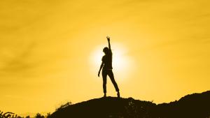 Silhouette of a person on a mountain top raising the pitchfork symbol.